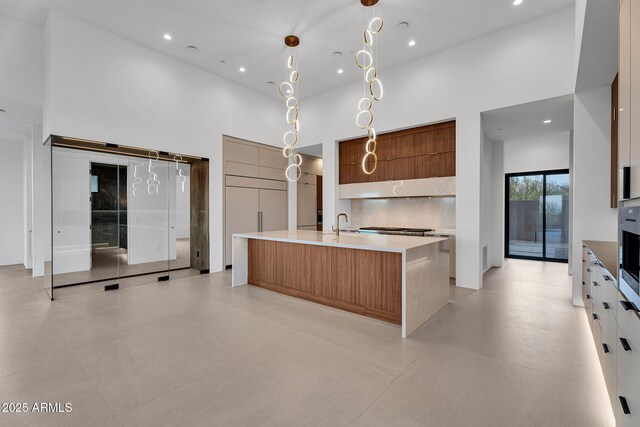 10354 E Celestial Dr, Scottsdale, AZ 85262 - kitchen featuring modern cabinets, a towering ceiling, an island with sink, decorative light fixtures, and brown cabinets