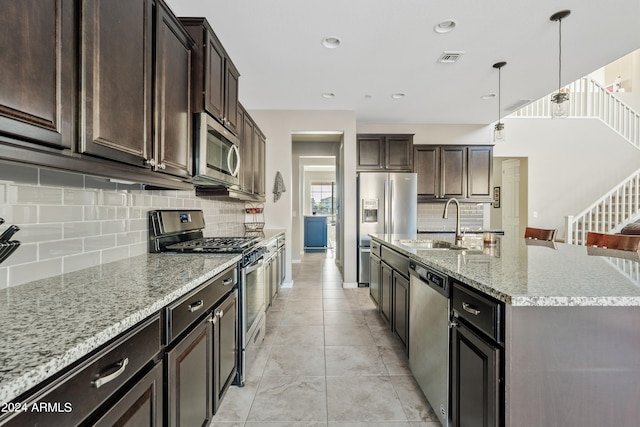 kitchen featuring tasteful backsplash, pendant lighting, light stone countertops, an island with sink, and appliances with stainless steel finishes