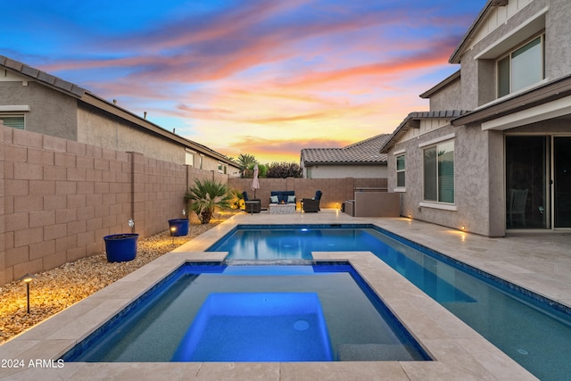 pool at dusk with an in ground hot tub and a patio