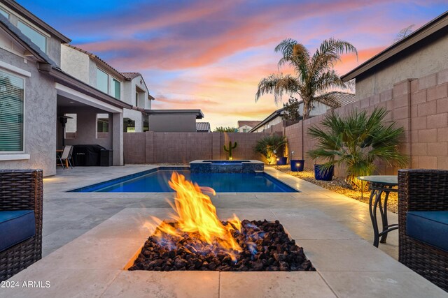 pool at dusk featuring an in ground hot tub, a patio area, and pool water feature