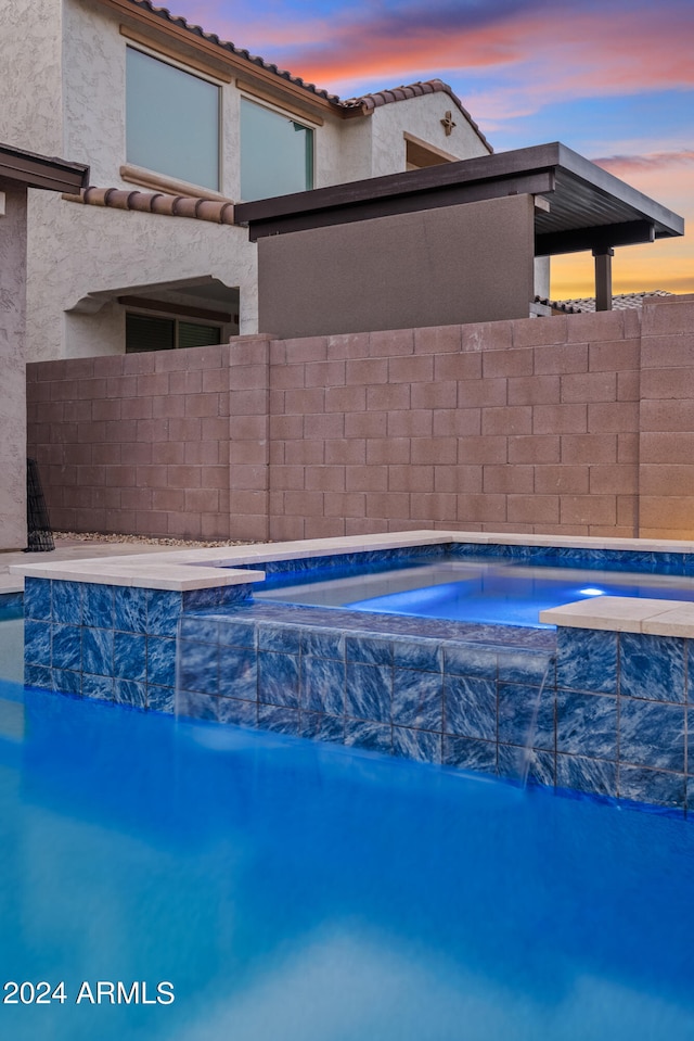 pool at dusk with an in ground hot tub