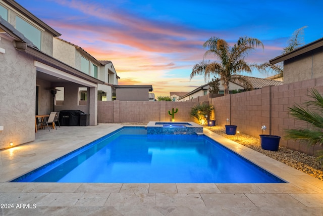 pool at dusk with an in ground hot tub and a patio area