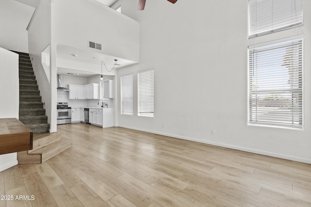 1225 N 36th St Unit 1015, Phoenix, AZ 85008 - unfurnished living room featuring a high ceiling, a ceiling fan, light wood finished floors, stairway, and baseboards