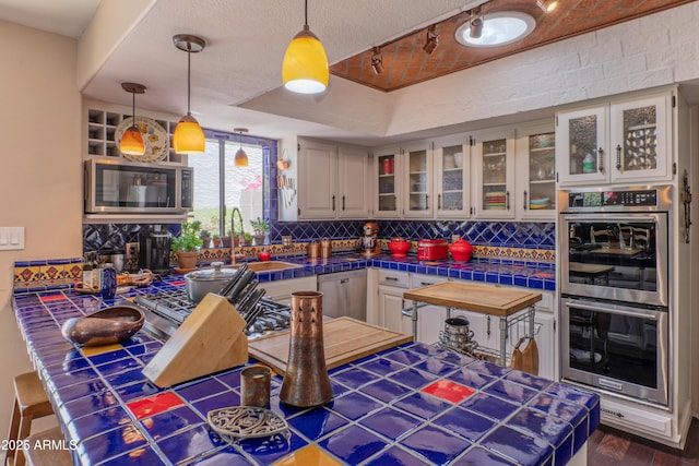 7302 E Rose Ln, Scottsdale, AZ 85250 - kitchen featuring stainless steel appliances, tile counters, decorative backsplash, glass insert cabinets, and a sink