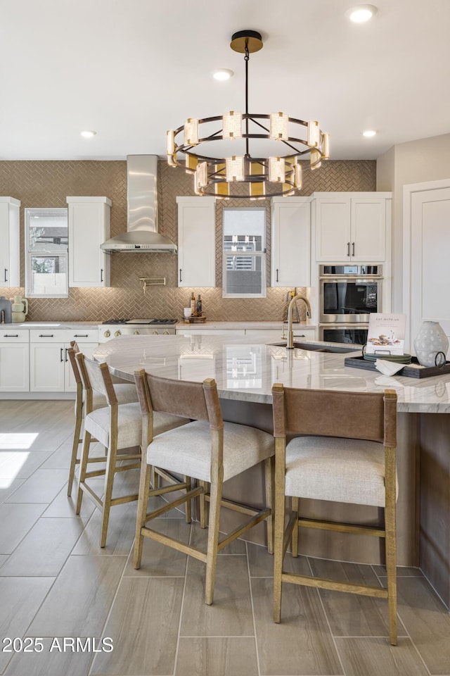 kitchen with a breakfast bar area, white cabinets, hanging light fixtures, and wall chimney exhaust hood