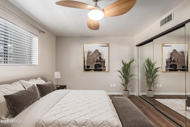 bedroom with wood finished floors, visible vents, a closet, and baseboards