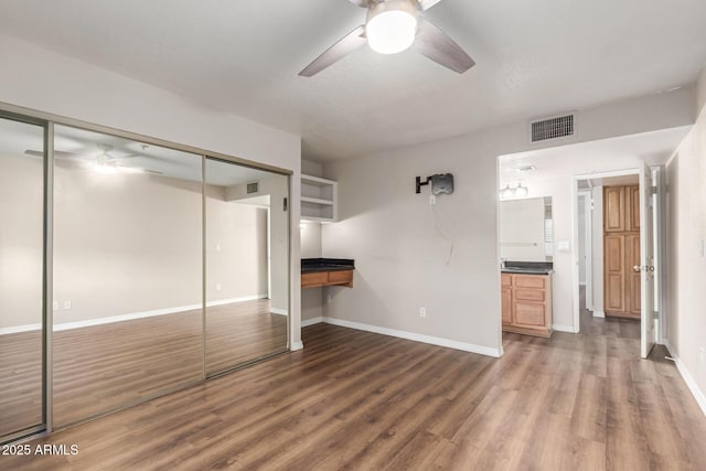 unfurnished bedroom with wood finished floors, visible vents, baseboards, ceiling fan, and a closet