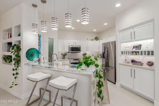 kitchen featuring a breakfast bar, kitchen peninsula, decorative light fixtures, white cabinetry, and stainless steel appliances