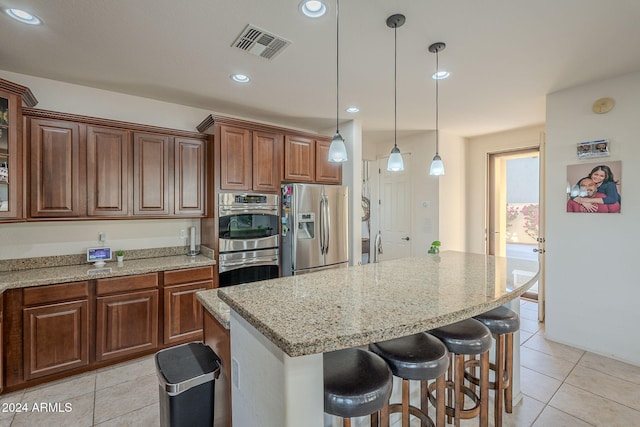 kitchen featuring light stone counters, a breakfast bar, stainless steel appliances, light tile patterned floors, and a center island