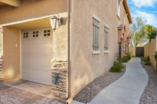 exterior space featuring a garage, stone siding, fence, and stucco siding