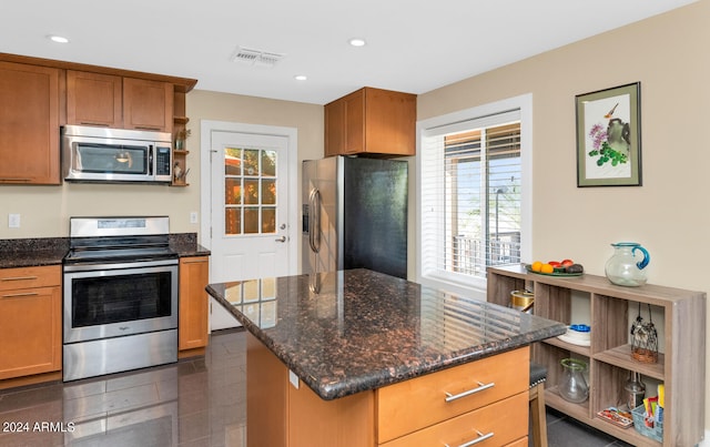 kitchen with dark tile patterned floors, a kitchen island, appliances with stainless steel finishes, and dark stone counters