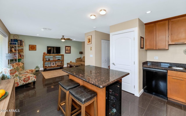 kitchen with black dishwasher, beverage cooler, ceiling fan, a kitchen breakfast bar, and dark stone counters