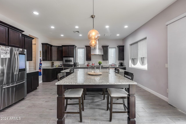 kitchen featuring light stone countertops, stainless steel appliances, decorative light fixtures, light hardwood / wood-style flooring, and a center island