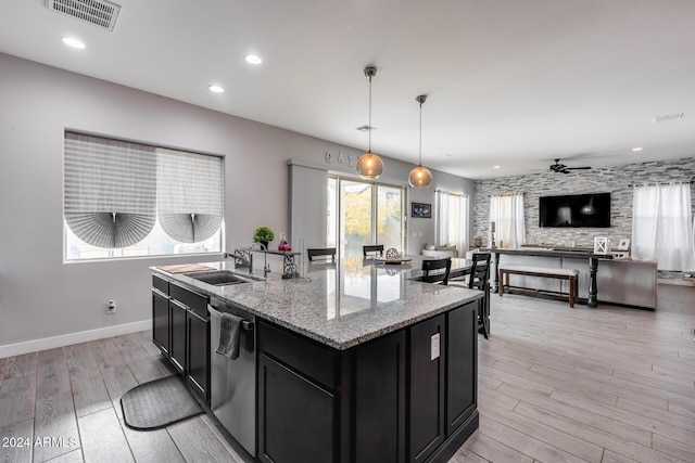 kitchen with ceiling fan, sink, stainless steel dishwasher, decorative light fixtures, and a center island with sink