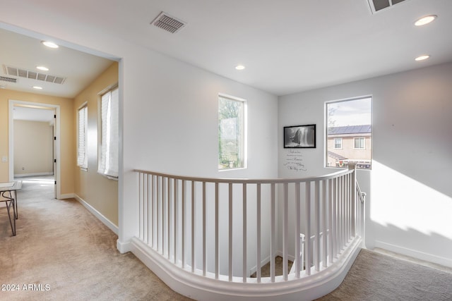 hall with a healthy amount of sunlight and light colored carpet