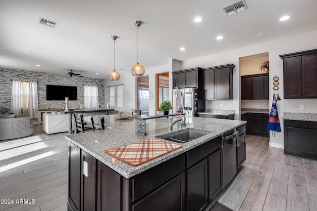 kitchen featuring light wood-type flooring, ceiling fan, sink, hanging light fixtures, and an island with sink