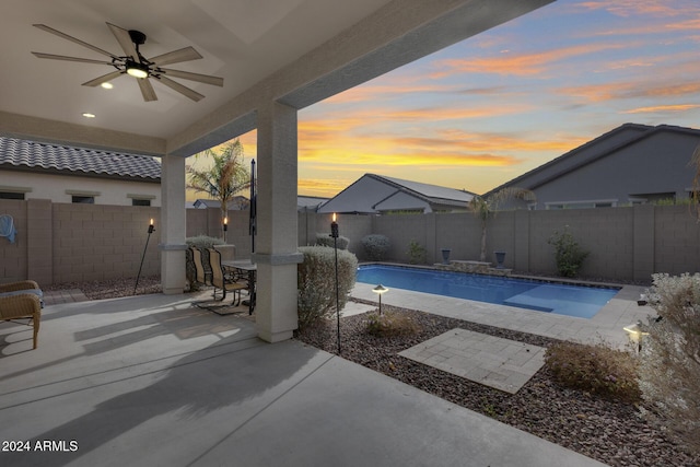 pool at dusk with ceiling fan and a patio area