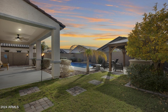 yard at dusk featuring a fenced in pool, ceiling fan, and a patio