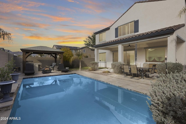 pool at dusk with a gazebo, ceiling fan, and a patio area