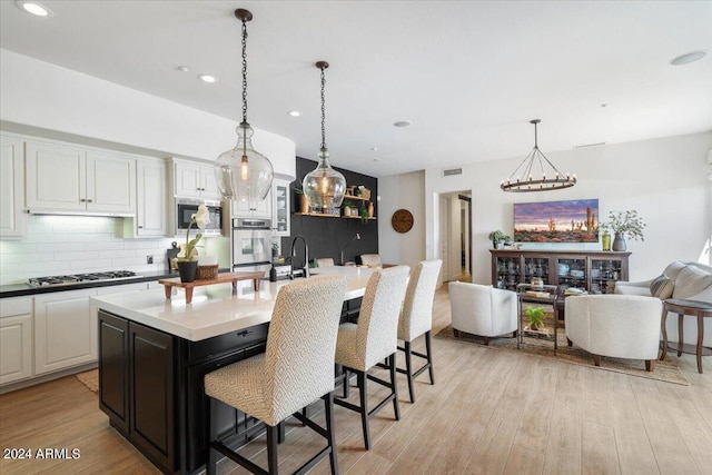 kitchen featuring a kitchen bar, decorative backsplash, hanging light fixtures, a center island with sink, and built in microwave