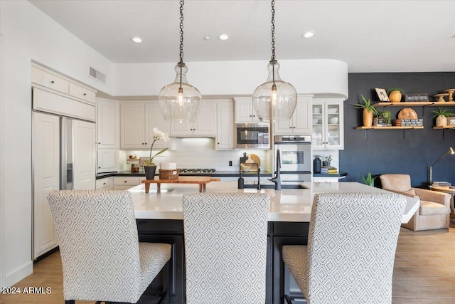 kitchen featuring tasteful backsplash, light wood-type flooring, built in appliances, pendant lighting, and a breakfast bar