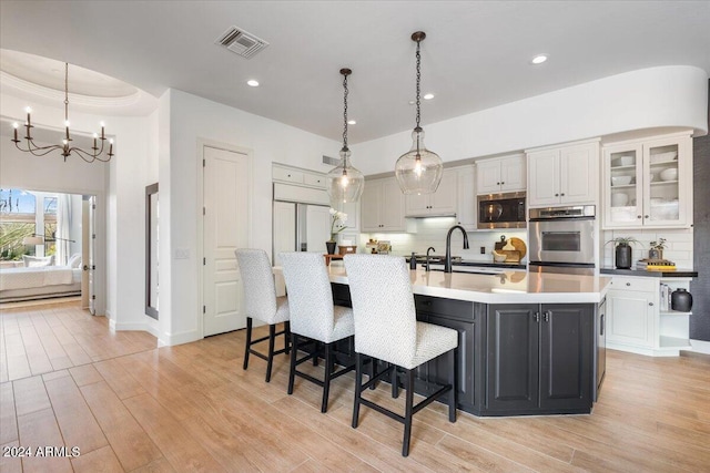 kitchen with white cabinetry, pendant lighting, built in microwave, and a kitchen island with sink