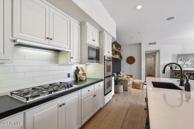 kitchen with backsplash, sink, white cabinetry, light wood-type flooring, and stainless steel appliances