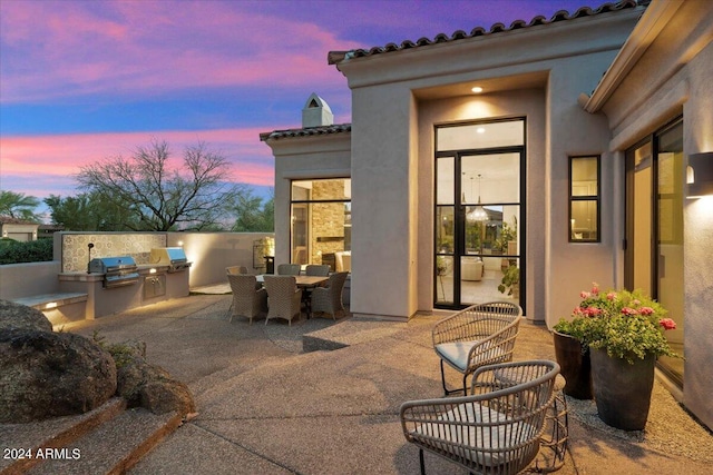 patio terrace at dusk featuring an outdoor kitchen and grilling area