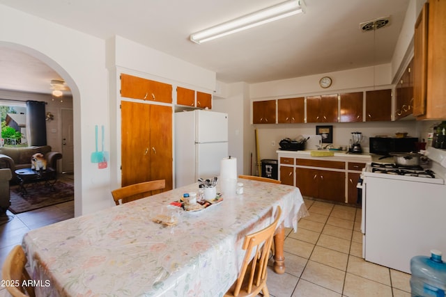 5637 N 63rd Dr, Glendale, AZ 85301 - kitchen featuring white appliances, light tile patterned floors, arched walkways, a kitchen bar, and brown cabinets