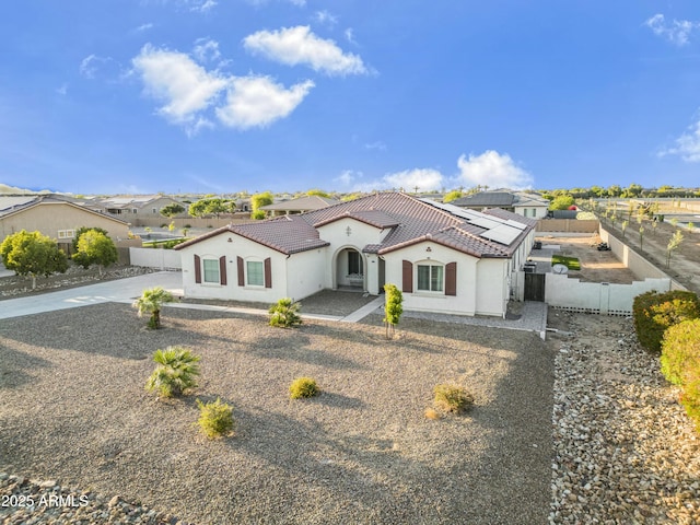 view of front facade with stucco siding, a tiled roof, fence, solar panels, and concrete driveway