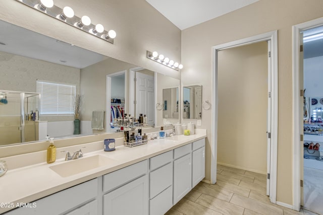 full bath featuring a walk in closet, a stall shower, double vanity, and a sink