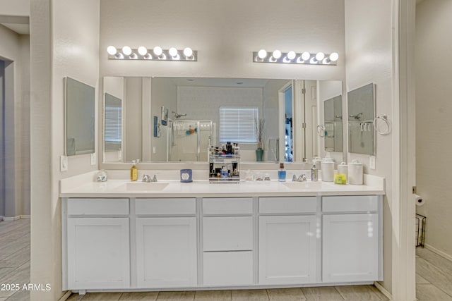 full bathroom featuring double vanity, baseboards, a stall shower, and a sink