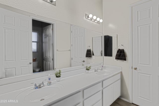 full bathroom with toilet, double vanity, and a sink