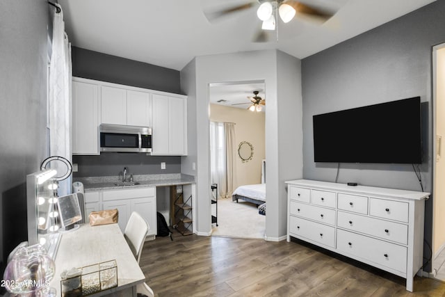 kitchen featuring dark wood finished floors, stainless steel microwave, ceiling fan, a sink, and white cabinetry