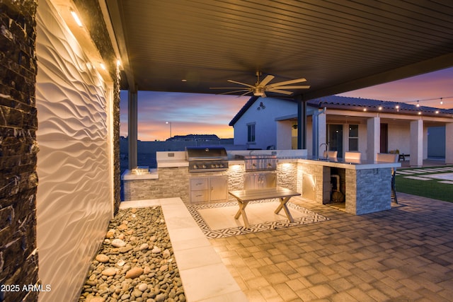patio terrace at dusk with area for grilling, a ceiling fan, and a grill
