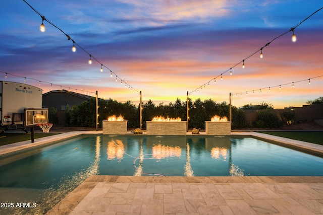 pool at dusk with a patio area and an outdoor pool