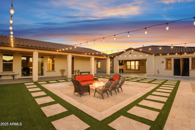 back of house at dusk featuring a patio, stucco siding, a tile roof, and an outdoor living space with a fire pit