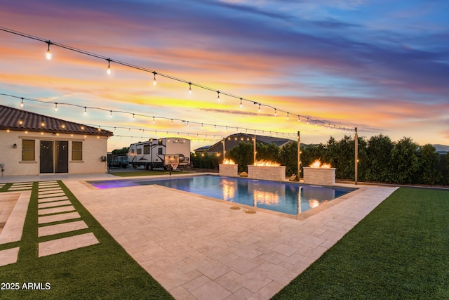 pool at dusk featuring an outdoor pool, a yard, and a patio