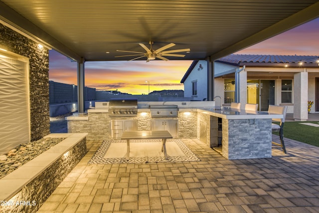 view of patio featuring a sink, outdoor wet bar, a grill, a ceiling fan, and exterior kitchen
