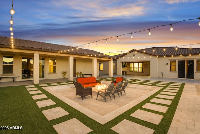 back of house at dusk with an outdoor living space with a fire pit, a patio, stucco siding, and a tiled roof