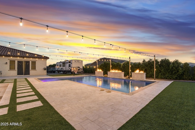 pool at dusk featuring an outdoor pool, a patio area, and a yard