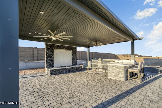 view of patio featuring a grill, a fenced backyard, a ceiling fan, an outdoor bar, and an outdoor kitchen