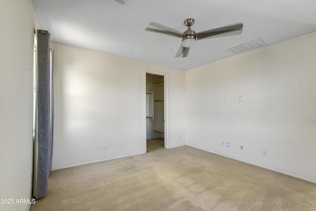 unfurnished bedroom featuring light colored carpet, visible vents, a ceiling fan, and a walk in closet