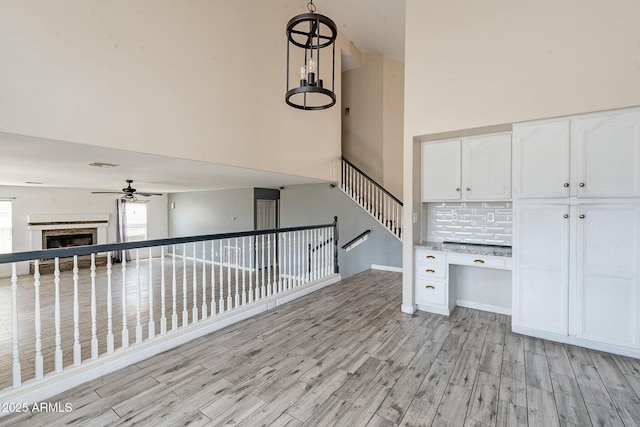 interior space with light wood-type flooring, baseboards, a towering ceiling, a ceiling fan, and a fireplace