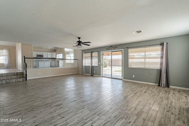 unfurnished living room with light wood-type flooring, baseboards, visible vents, and a ceiling fan