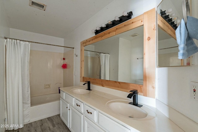 bathroom featuring visible vents, a sink, double vanity, and wood finished floors