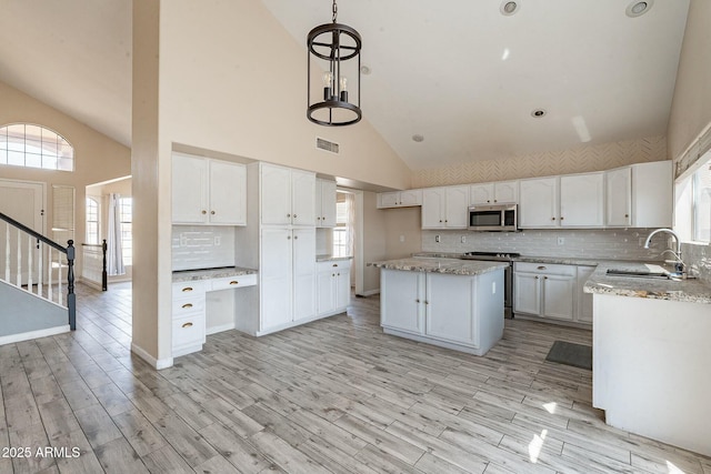 kitchen with a sink, appliances with stainless steel finishes, light stone counters, and visible vents
