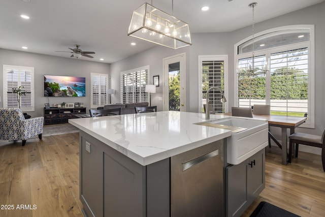 kitchen with sink, gray cabinetry, light stone counters, hanging light fixtures, and a center island with sink