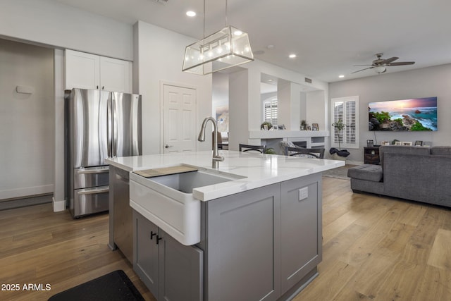 kitchen featuring pendant lighting, gray cabinets, stainless steel appliances, light stone counters, and a center island with sink