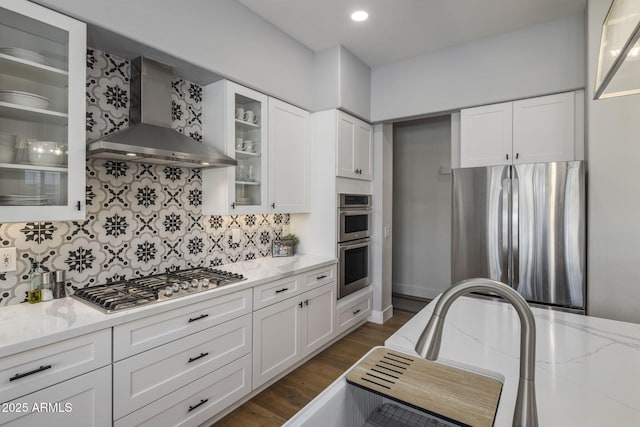 kitchen with stainless steel appliances, light stone countertops, white cabinets, and wall chimney exhaust hood